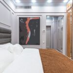 Contemporary hotel room interior with pillows and cover on bed against artwork on wall and light corridor